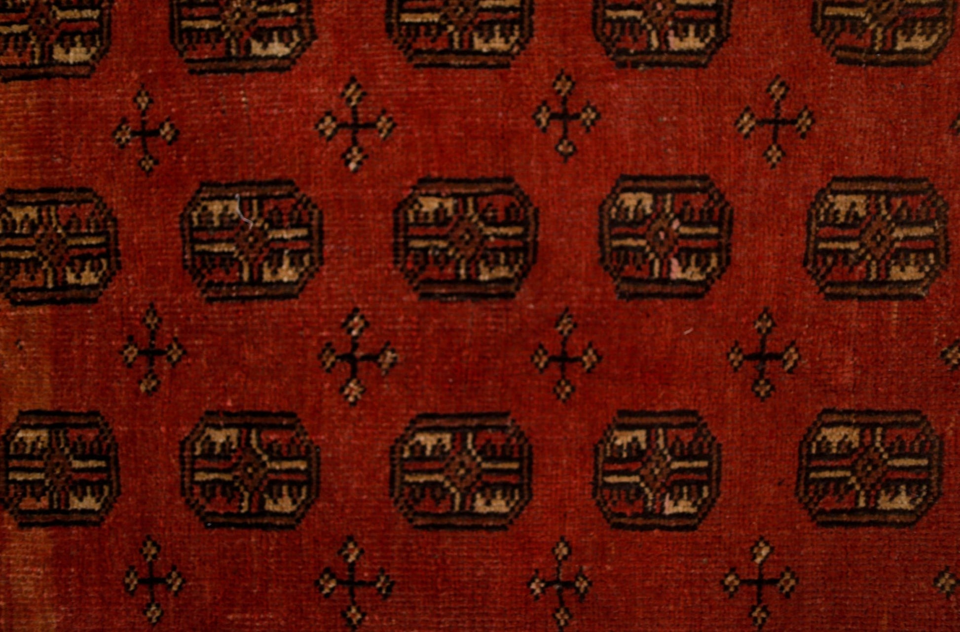 A vintage handwoven Afghan rug featuring a repeating geometric pattern on a deep red background.