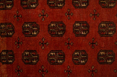 A vintage handwoven Afghan rug featuring a repeating geometric pattern on a deep red background.