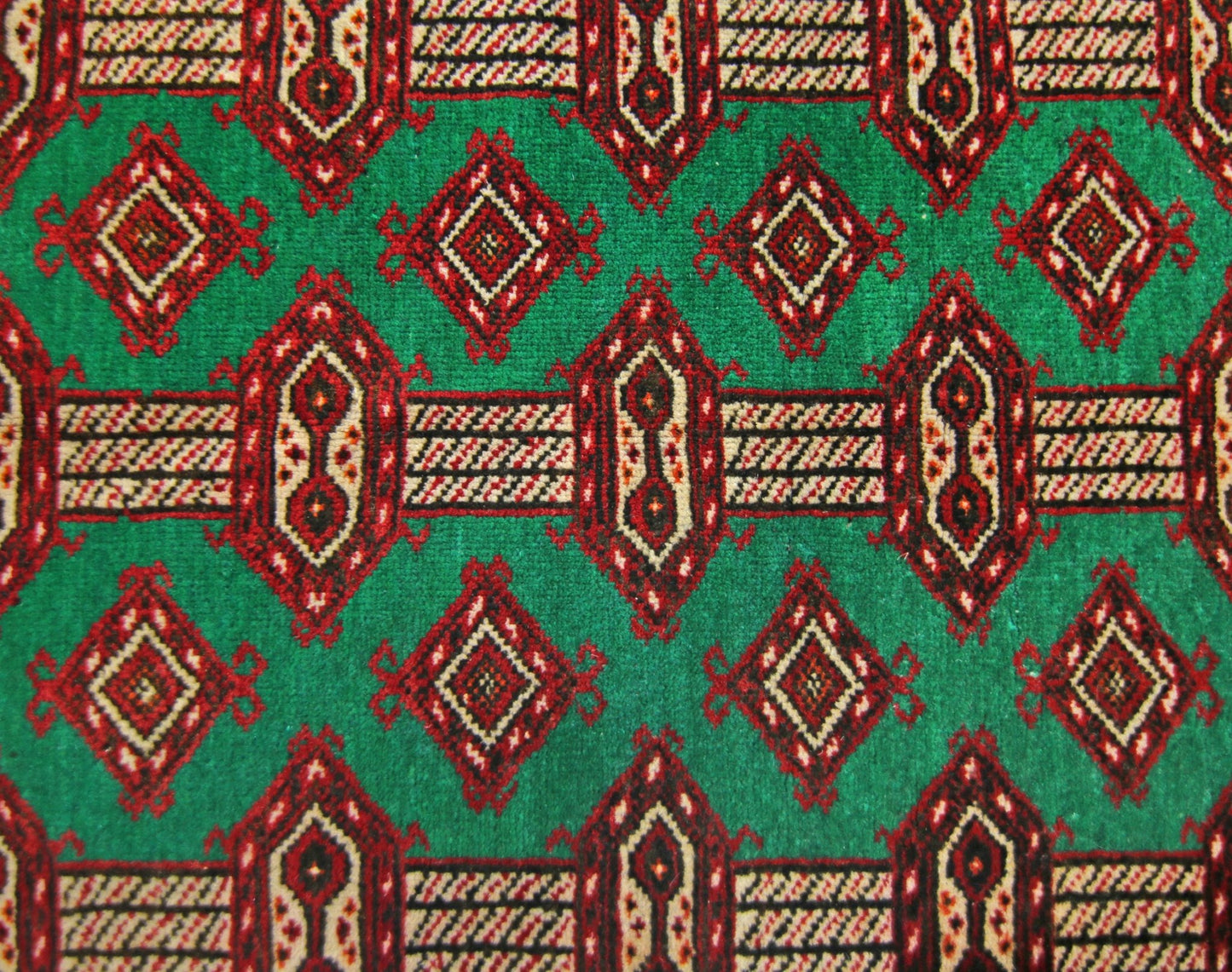 A vintage Persian Turkmen rug featuring a repeating geometric pattern in red and cream on a green field.