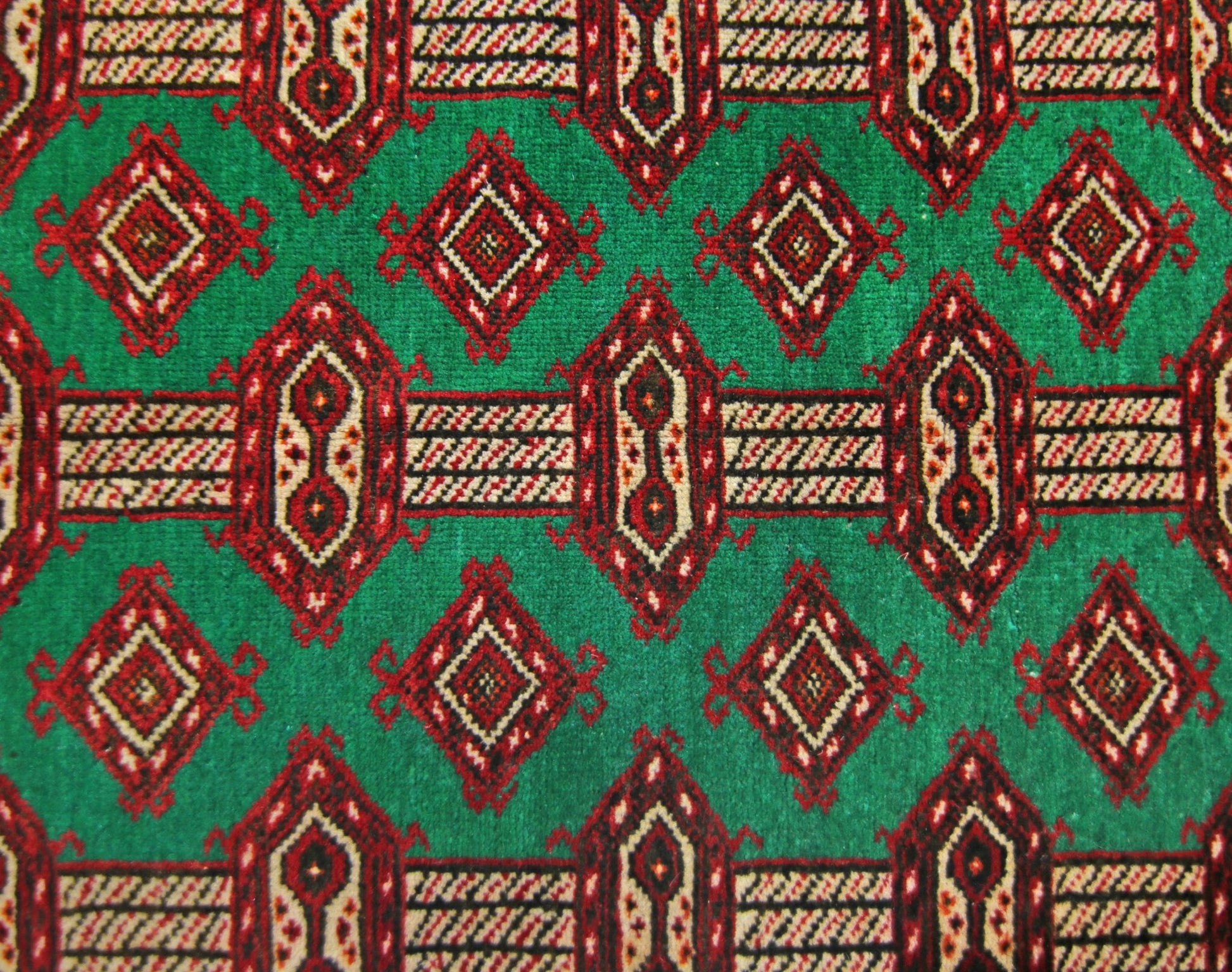 A vintage Persian Turkmen rug featuring a repeating geometric pattern in red and cream on a green field.