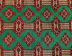 A vintage Persian Turkmen rug featuring a repeating geometric pattern in red and cream on a green field.