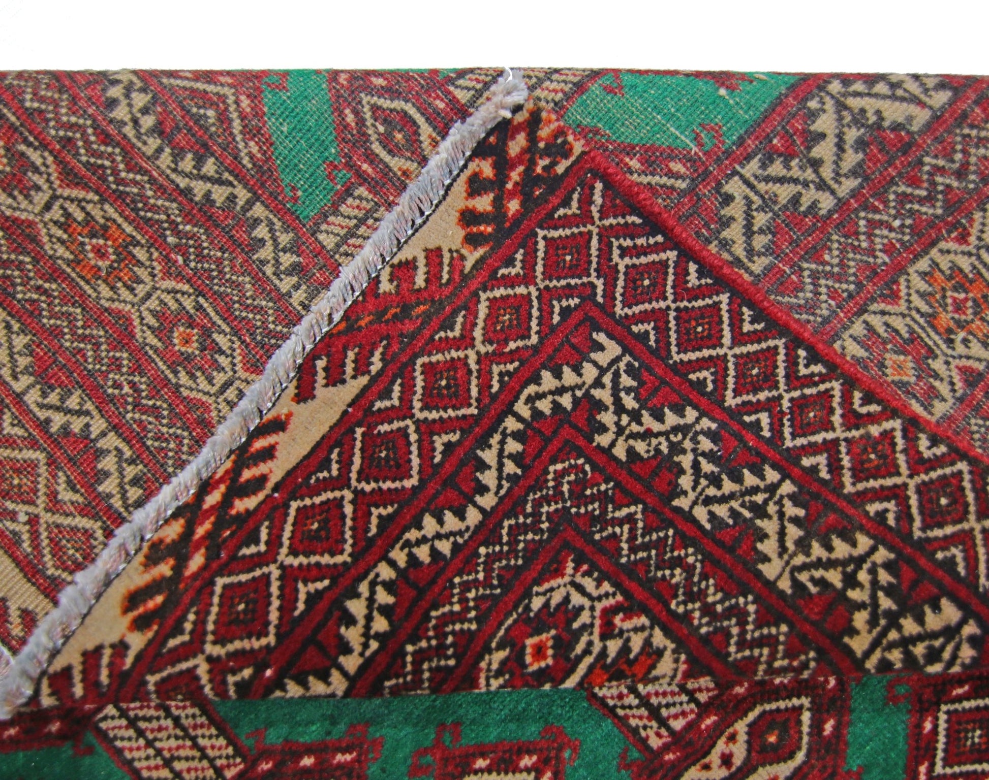 A close-up view of a vintage Persian Turkmen rug showing its intricate red and green geometric pattern.