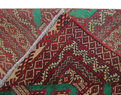 A close-up view of a vintage Persian Turkmen rug showing its intricate red and green geometric pattern.