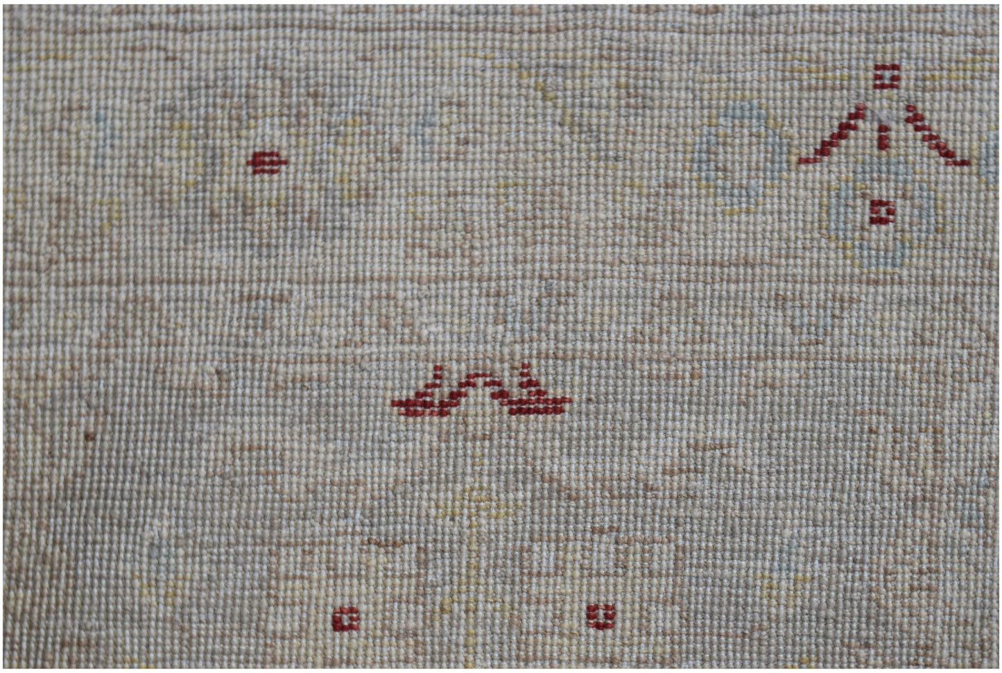 A close-up of an Afghan Chobi runner featuring a beige wool pile with small red geometric motifs.