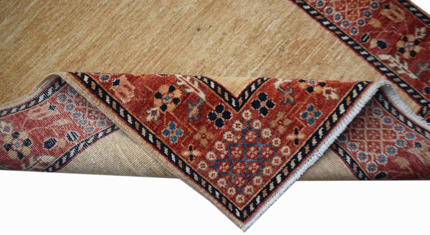 A handwoven Afghan Chobi runner with a tan field and a red patterned border folded over.