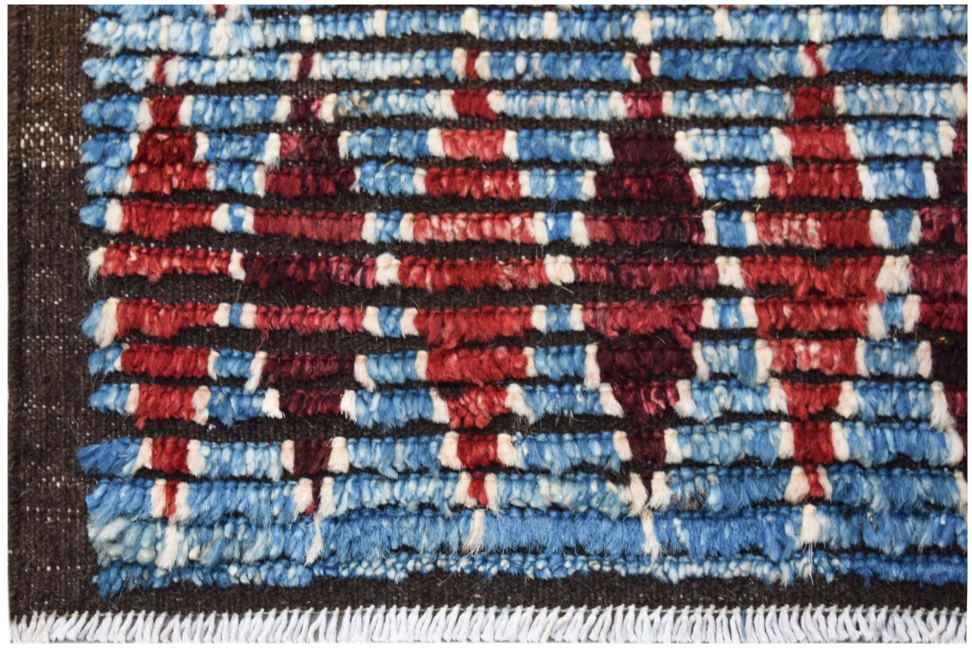 A hand-knotted Afghan rug featuring a geometric pattern in blue, red, and white wool.