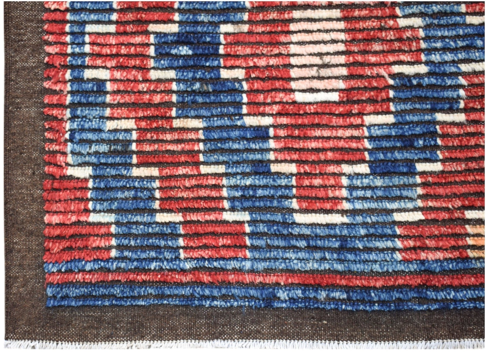 A hand-knotted Afghan rug featuring a geometric pattern in red, blue, and cream wool.