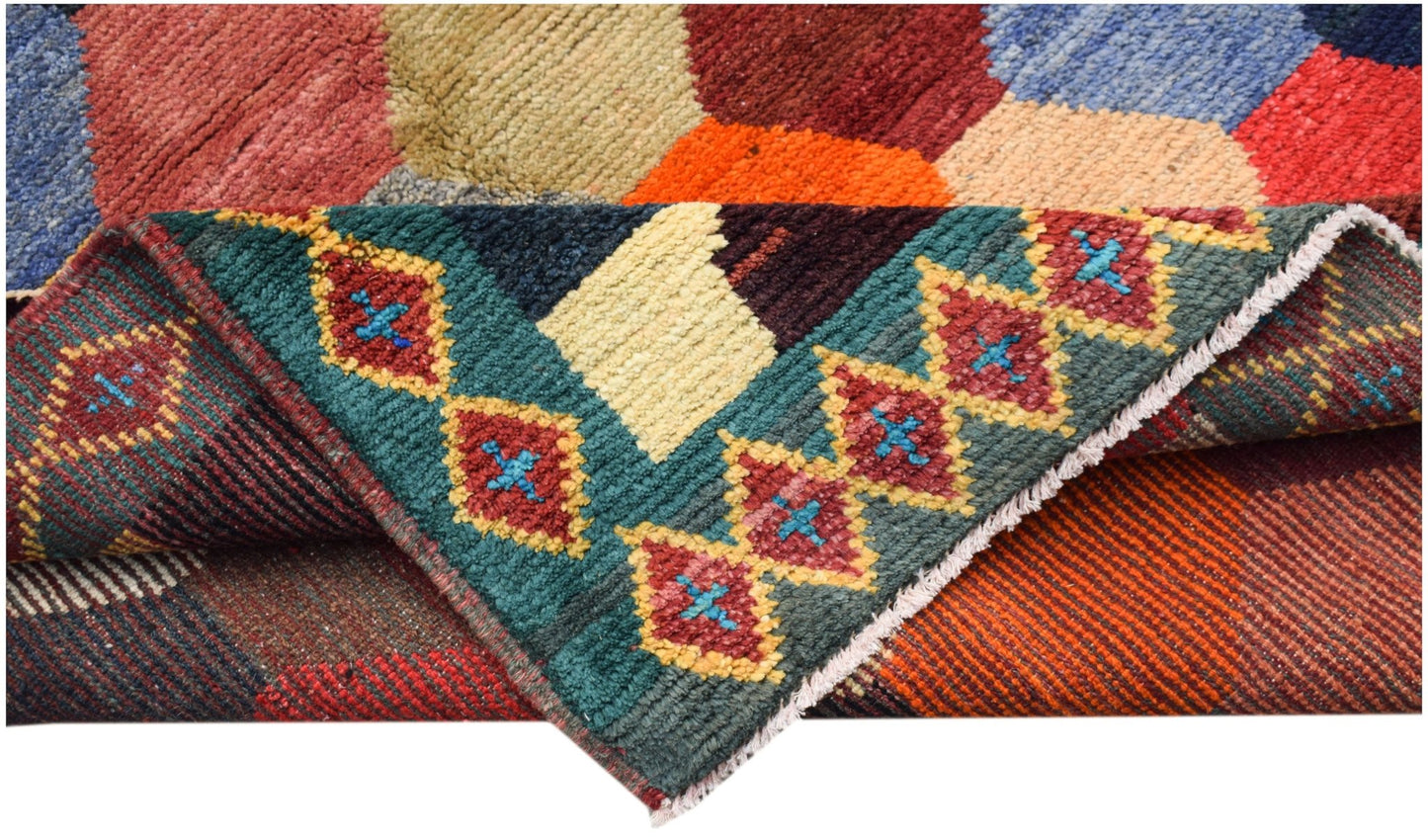 A hand-knotted Afghan wool rug featuring a colorful geometric pattern and a folded corner.