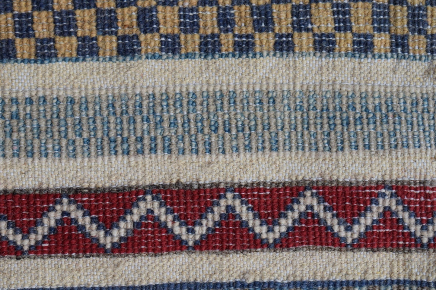 A close-up of a handmade Afghan runner rug featuring geometric patterns in blue, red, and cream.