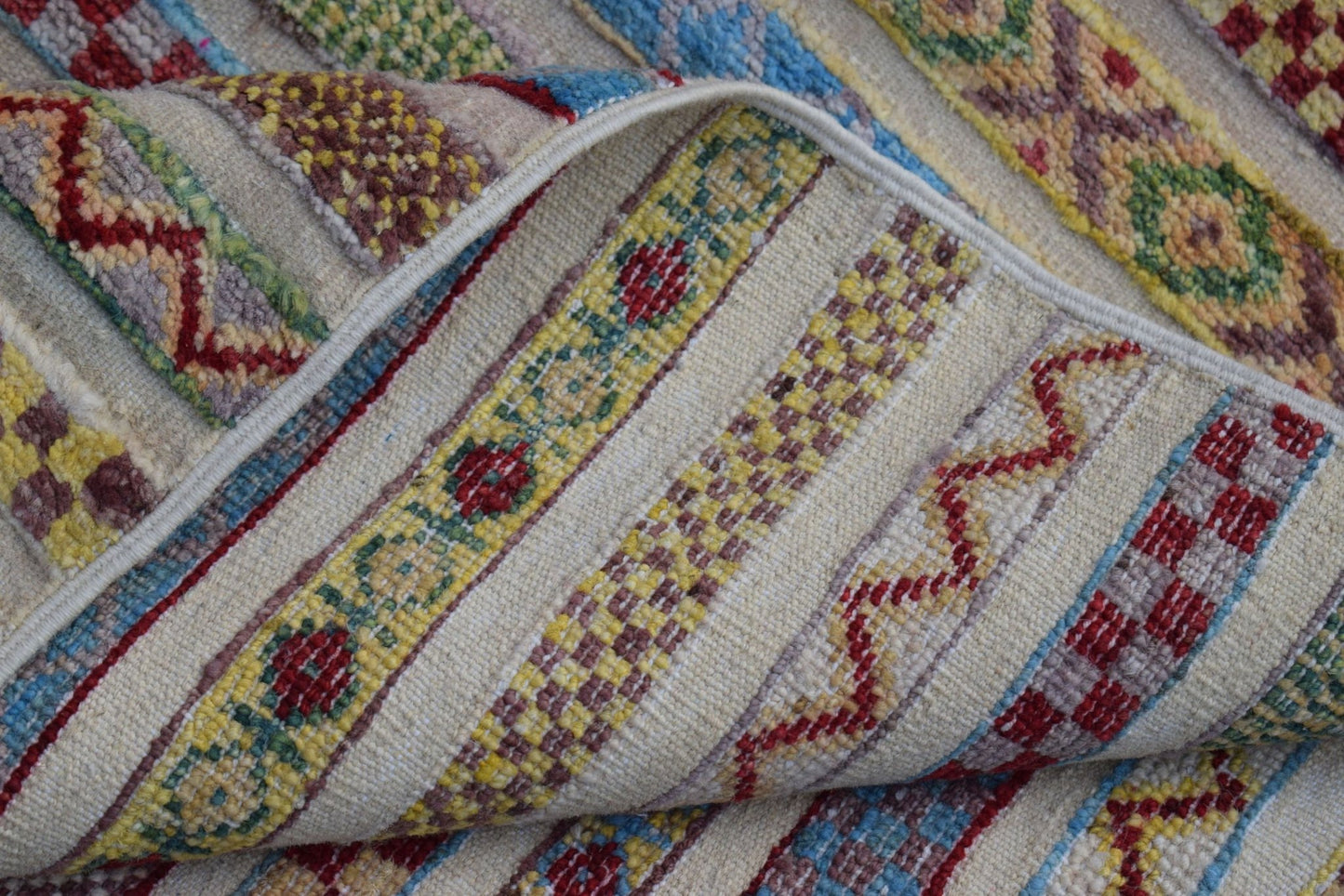 A folded Afghan Yekta rug featuring colorful geometric patterns and floral motifs on a cream base.