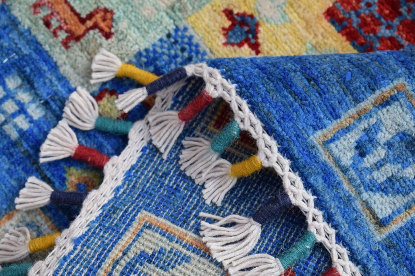 A close-up of a handmade Afghan Chobi runner featuring a blue field and decorative tassel fringe.