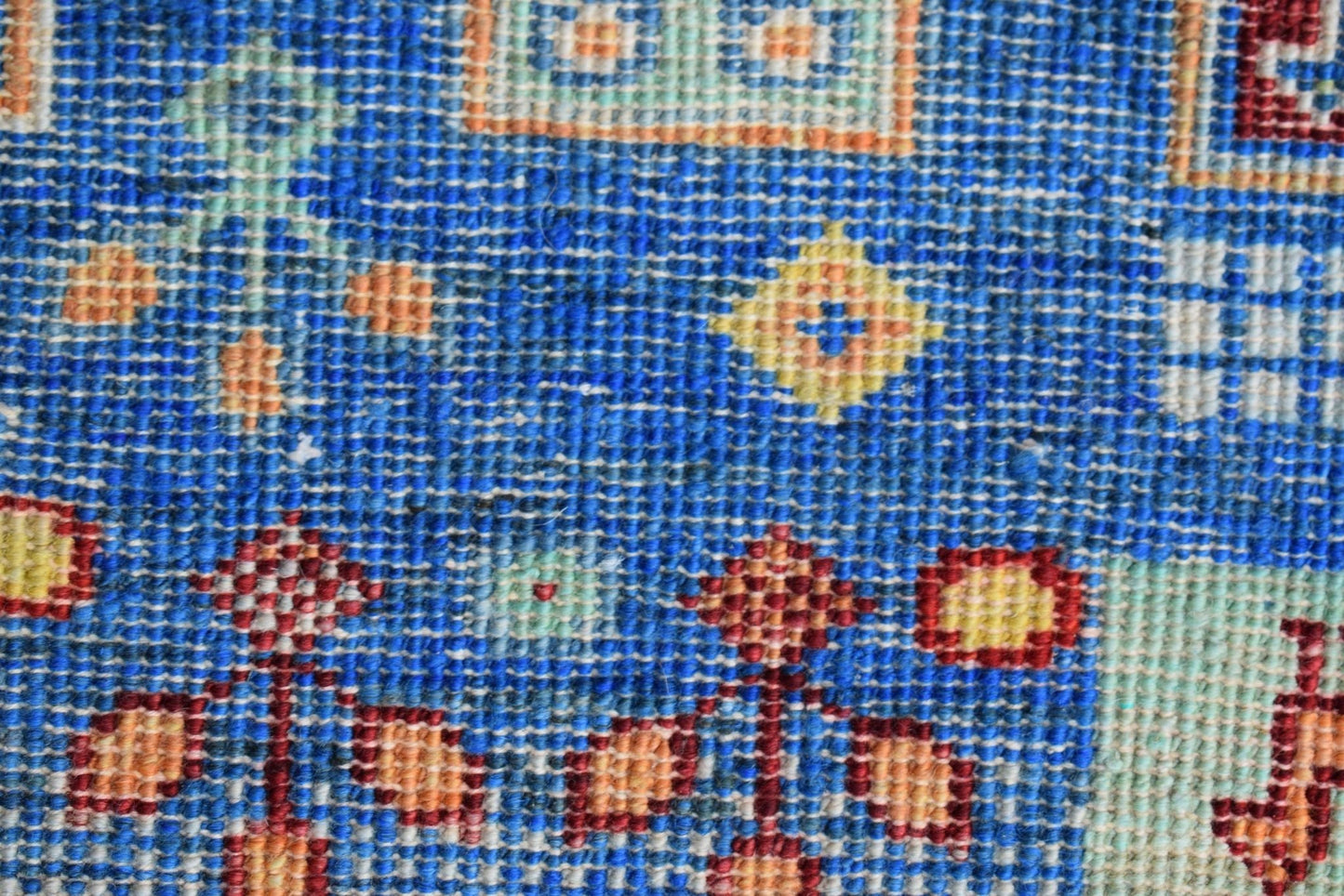 A close-up of a handmade Afghan Chobi runner featuring intricate geometric patterns in blue and red.