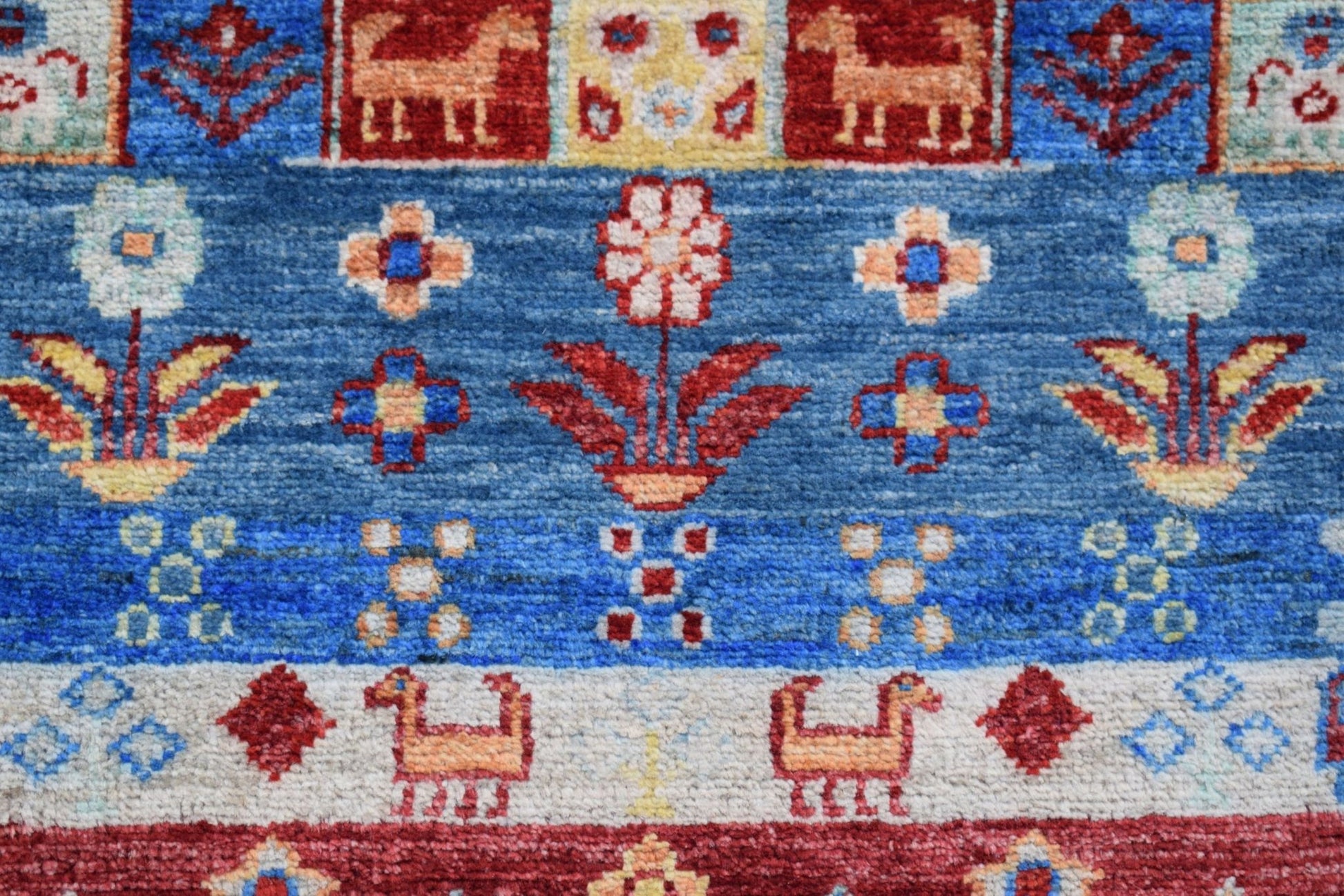A handmade Afghan Chobi runner featuring stylized animal and floral motifs in blue and red tones.