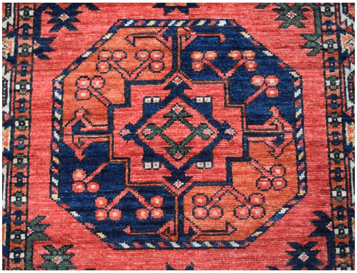 A handwoven Afghan Chobi runner featuring a geometric medallion pattern in red, blue, and orange.