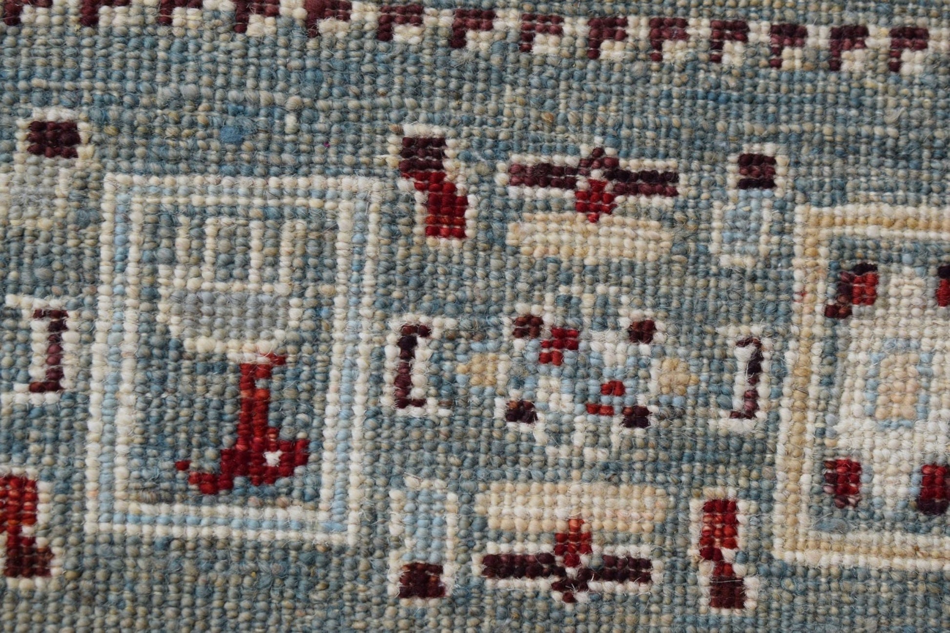 A close-up of a handmade Afghan Chobi runner featuring intricate geometric patterns in blue and red.