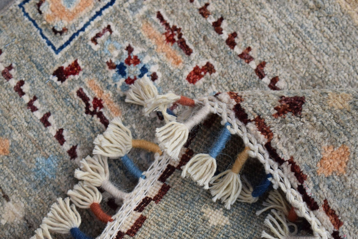 A close-up of a handmade Afghan Chobi runner featuring a wool pile and decorative knotted fringe.