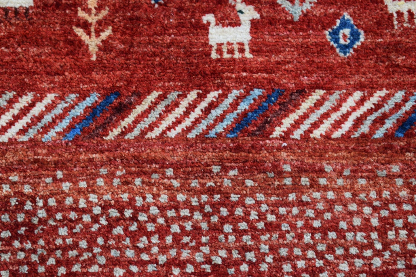 A handmade Afghan Chobi runner featuring a red wool pile with white animal and geometric motifs.