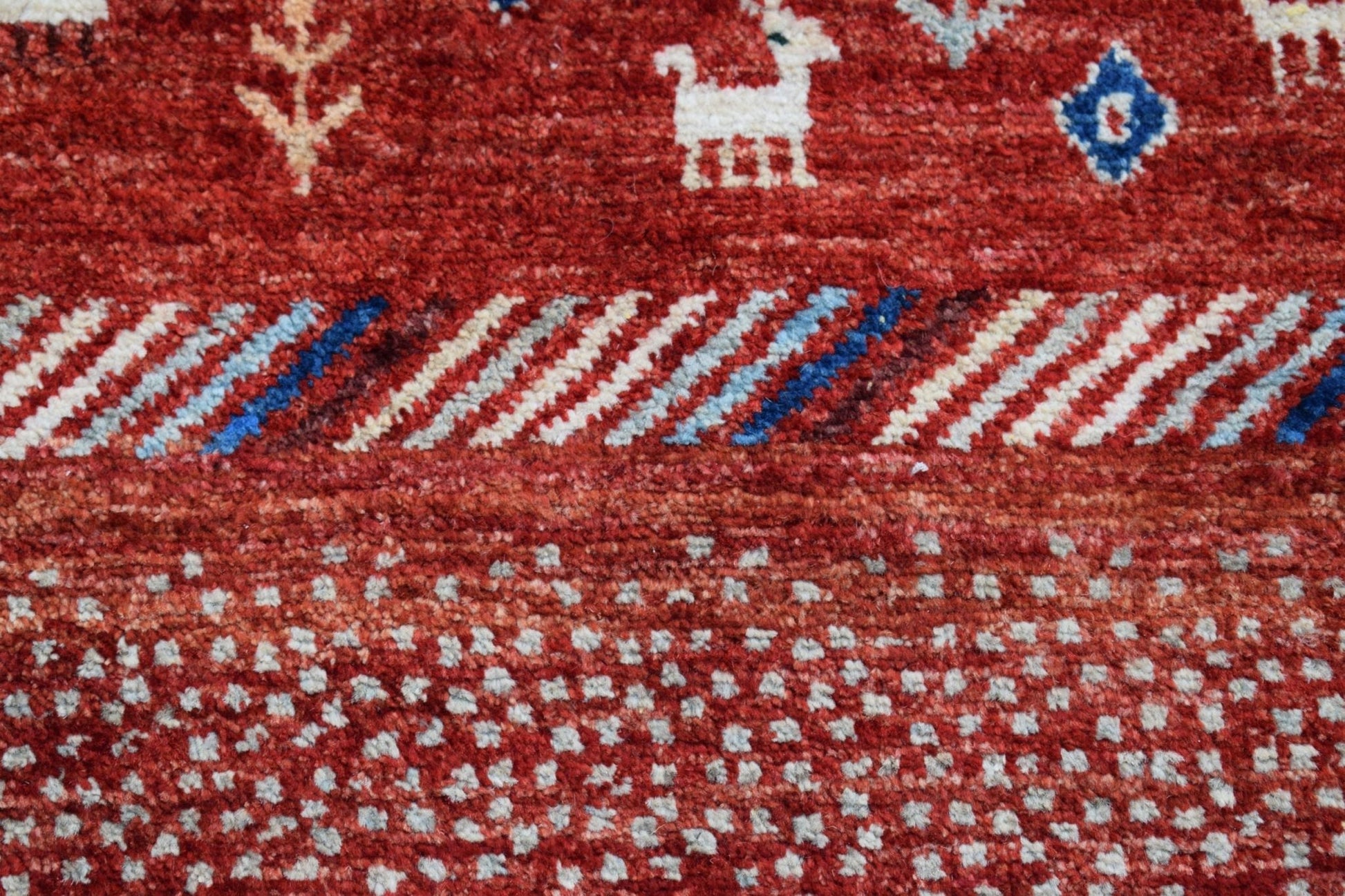 A handmade Afghan Chobi runner featuring a red wool pile with white animal and geometric motifs.