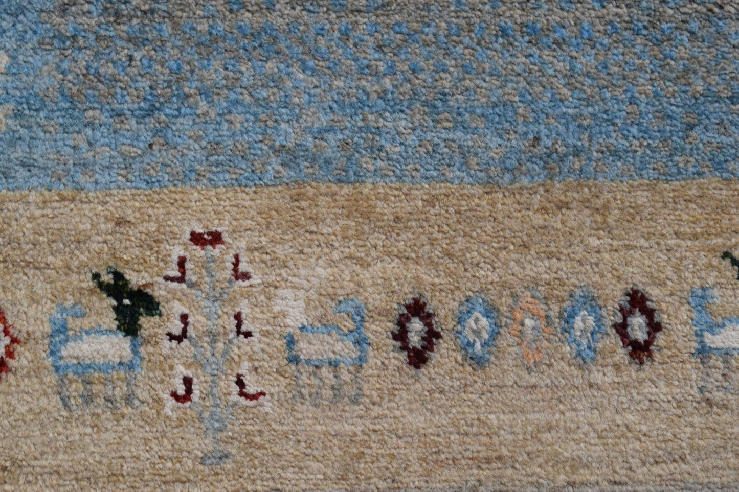A close-up of a handmade Afghan Chobi runner featuring a beige field with stylized animal motifs.