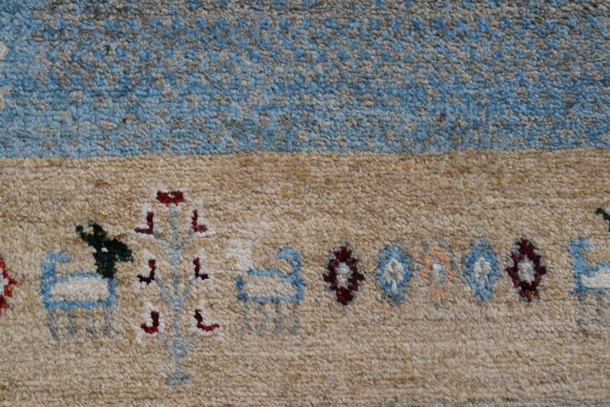 A close-up of a handmade Afghan Chobi runner featuring a beige field with stylized animal motifs.