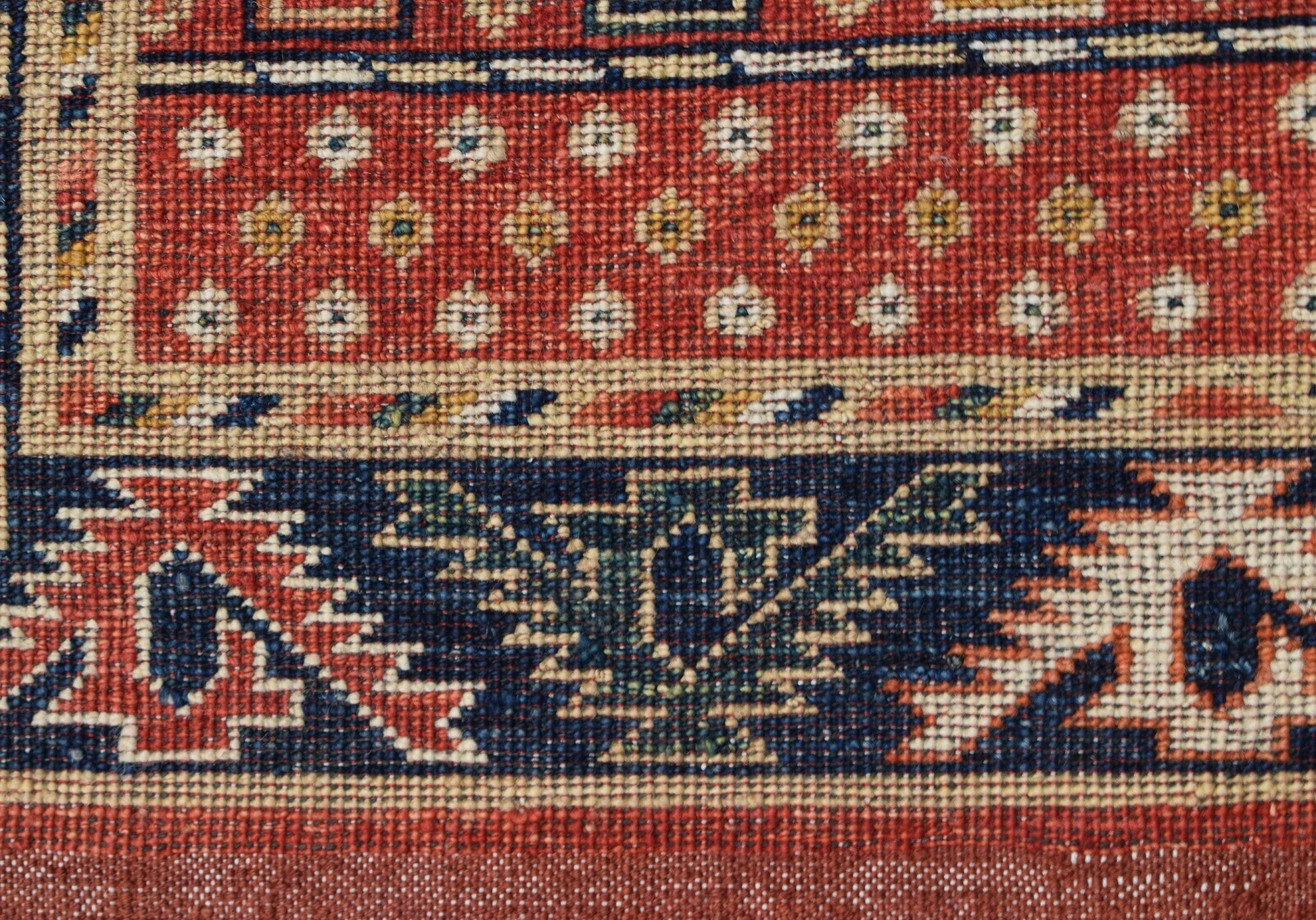 A close-up of a handwoven Afghan Chobi runner featuring geometric patterns in red, blue, and cream.