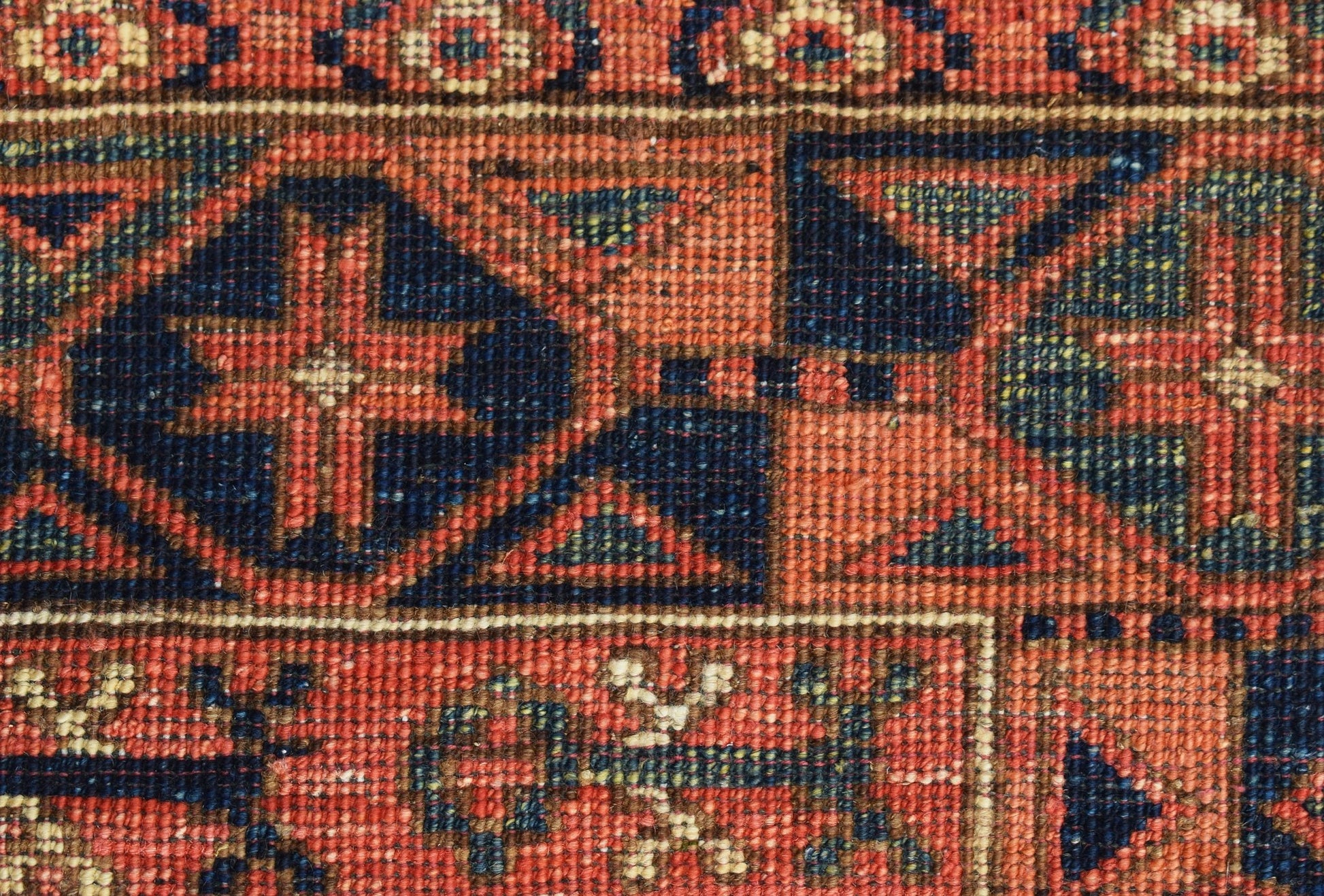 A close-up of a handwoven Afghan Chobi rug featuring geometric patterns in earthy red and blue tones.