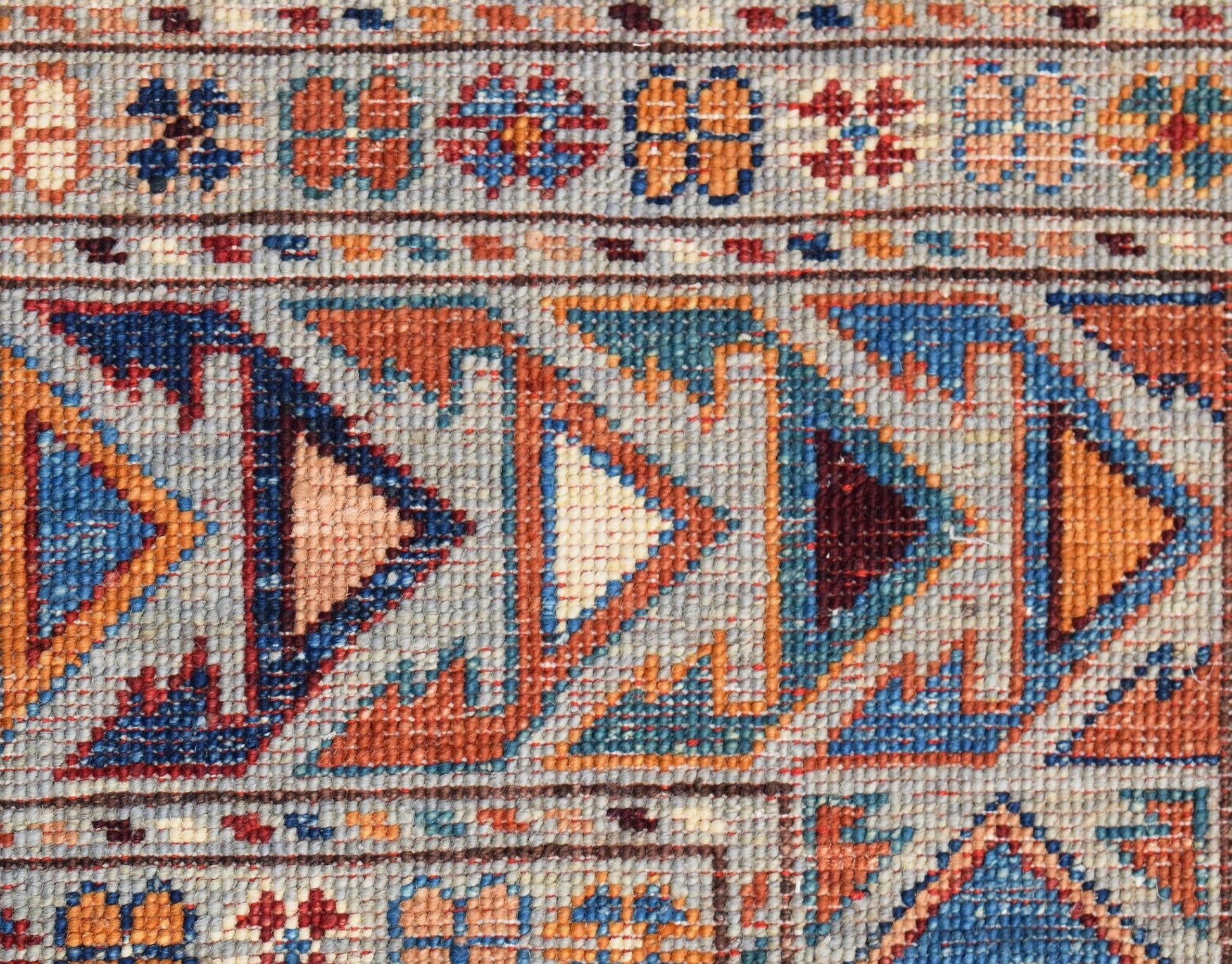 A close-up of an Afghan Chobi rug featuring geometric triangular patterns in blue and orange tones.