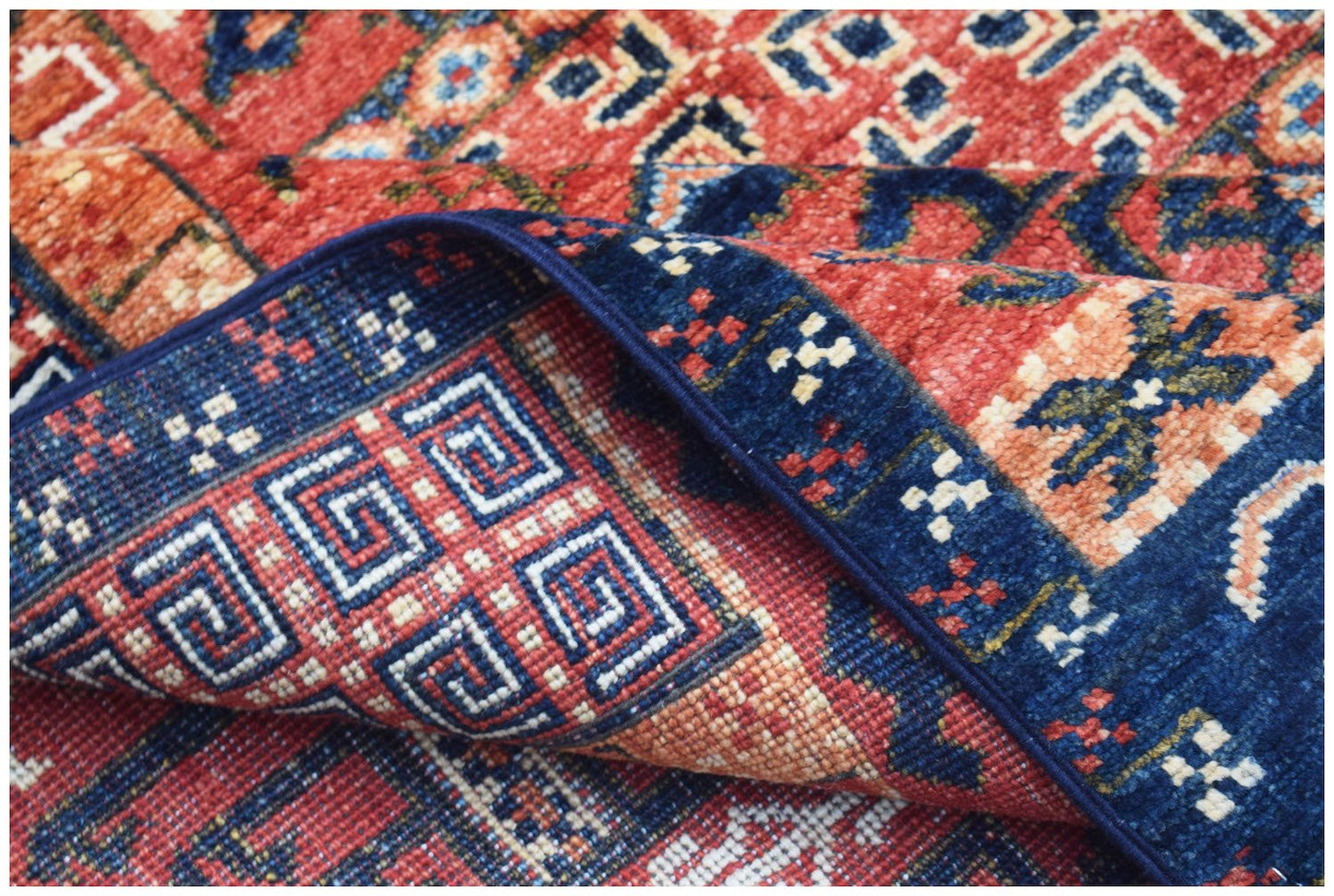 A handwoven Afghan Chobi rug featuring a traditional geometric pattern in red and blue tones.