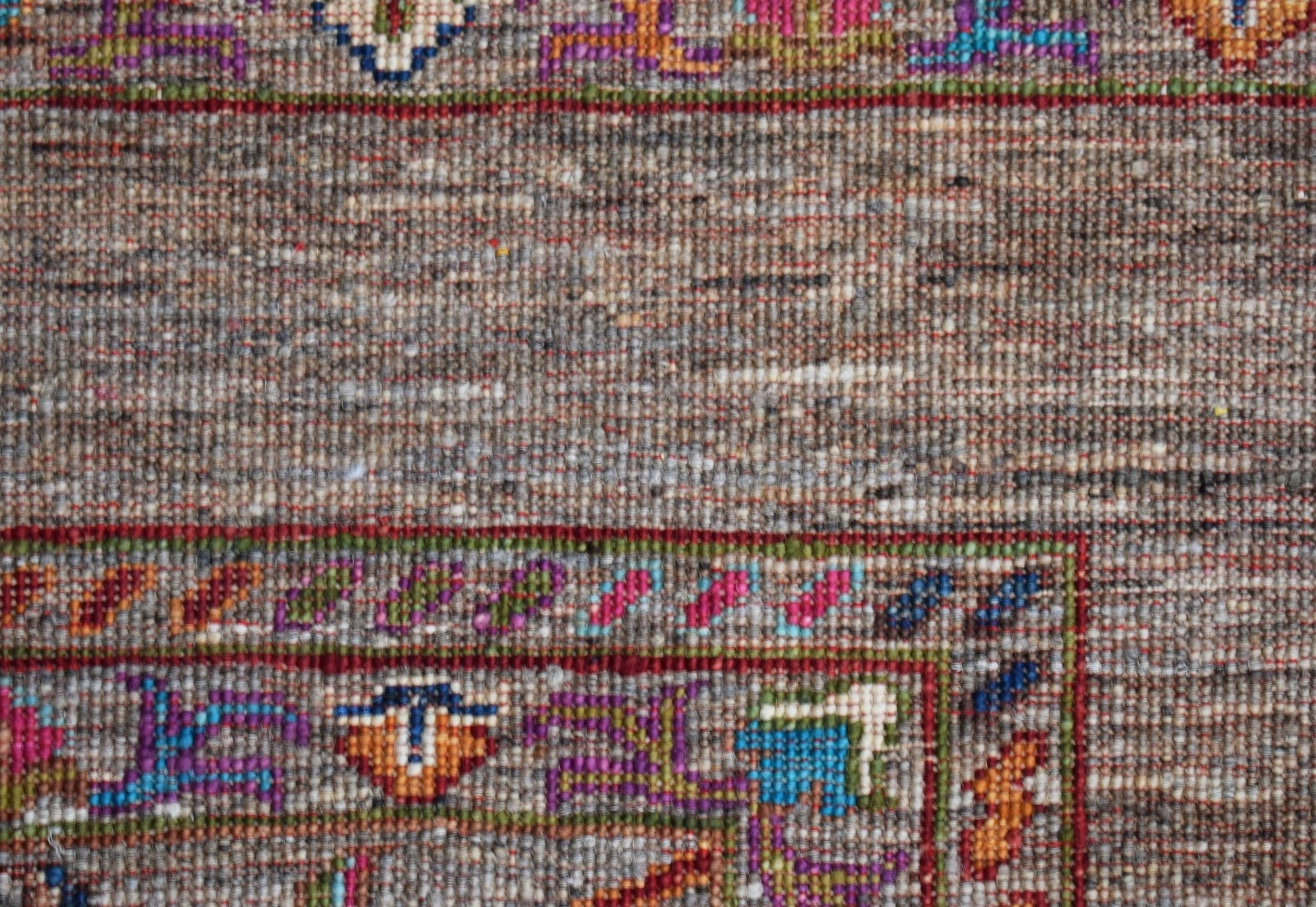 A close-up of a handwoven Afghan Chobi rug featuring a textured brown field and colorful borders.