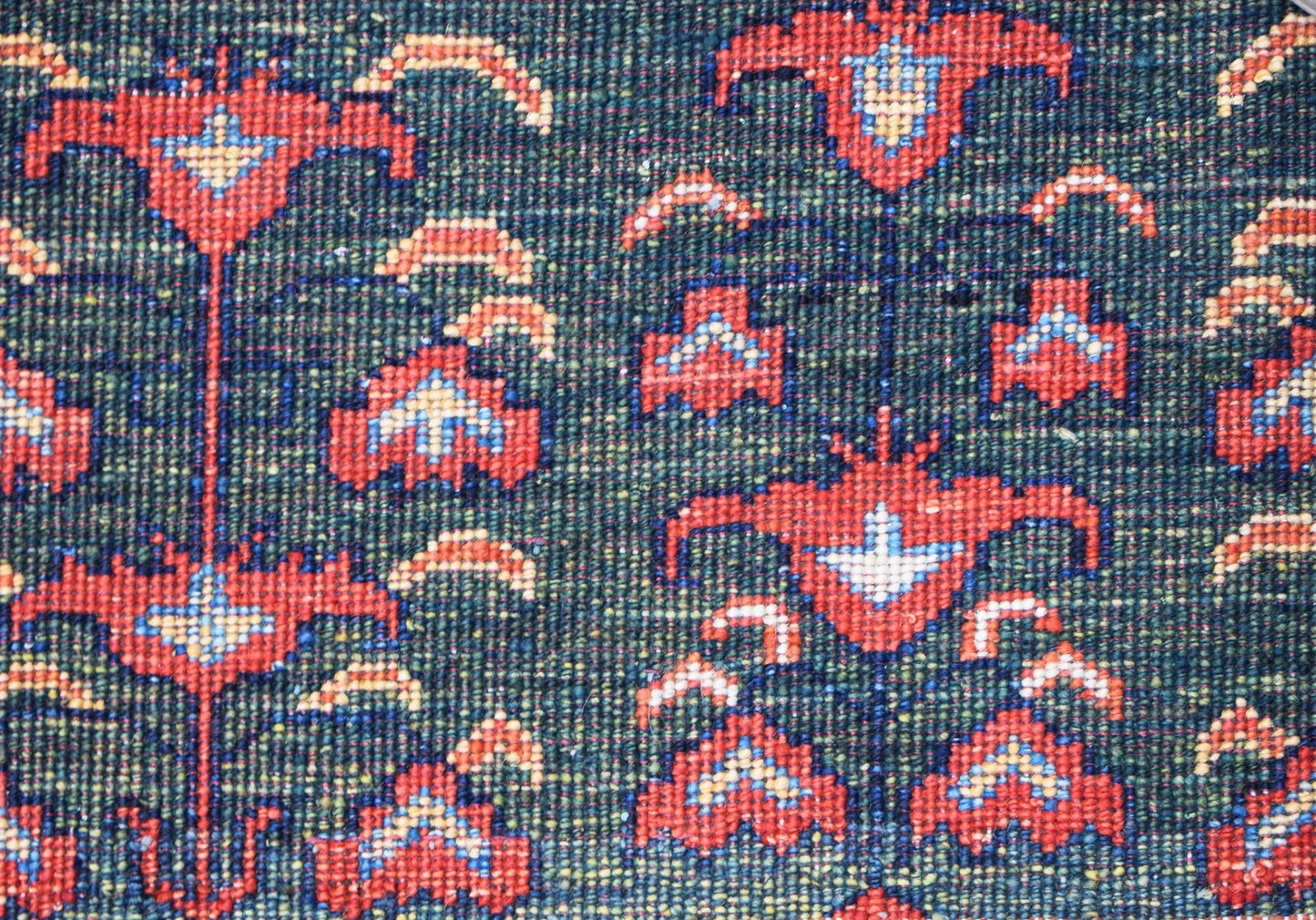 A close-up of an Afghan Chobi rug featuring a repeating floral pattern in red and blue on green.