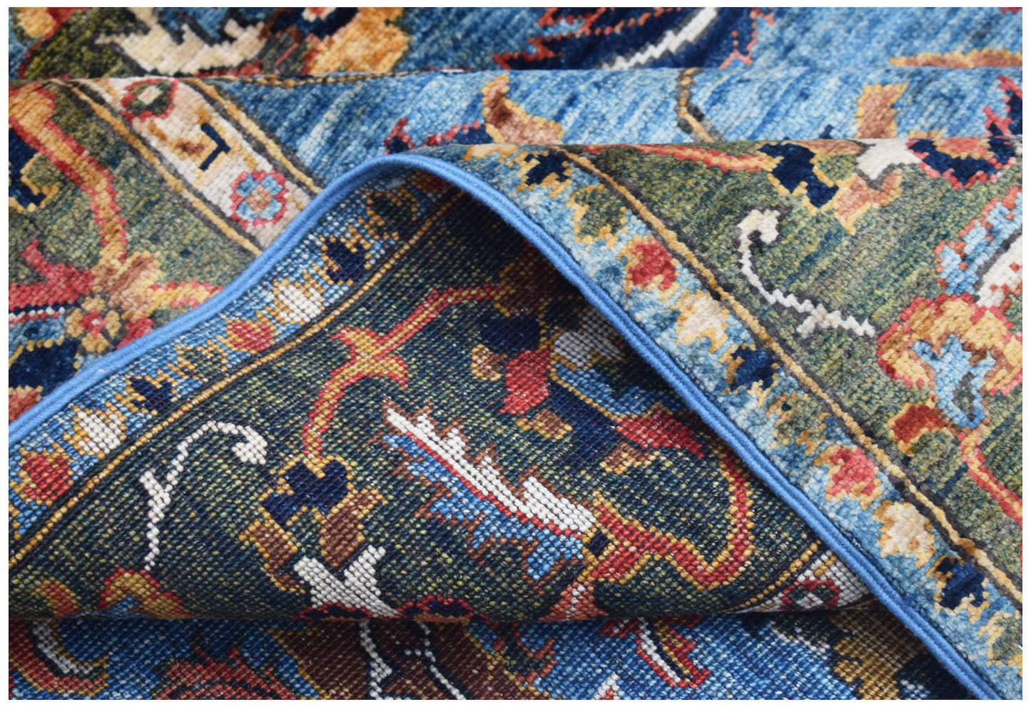A folded Afghan Chobi rug featuring intricate traditional patterns in blue, green, and red tones.