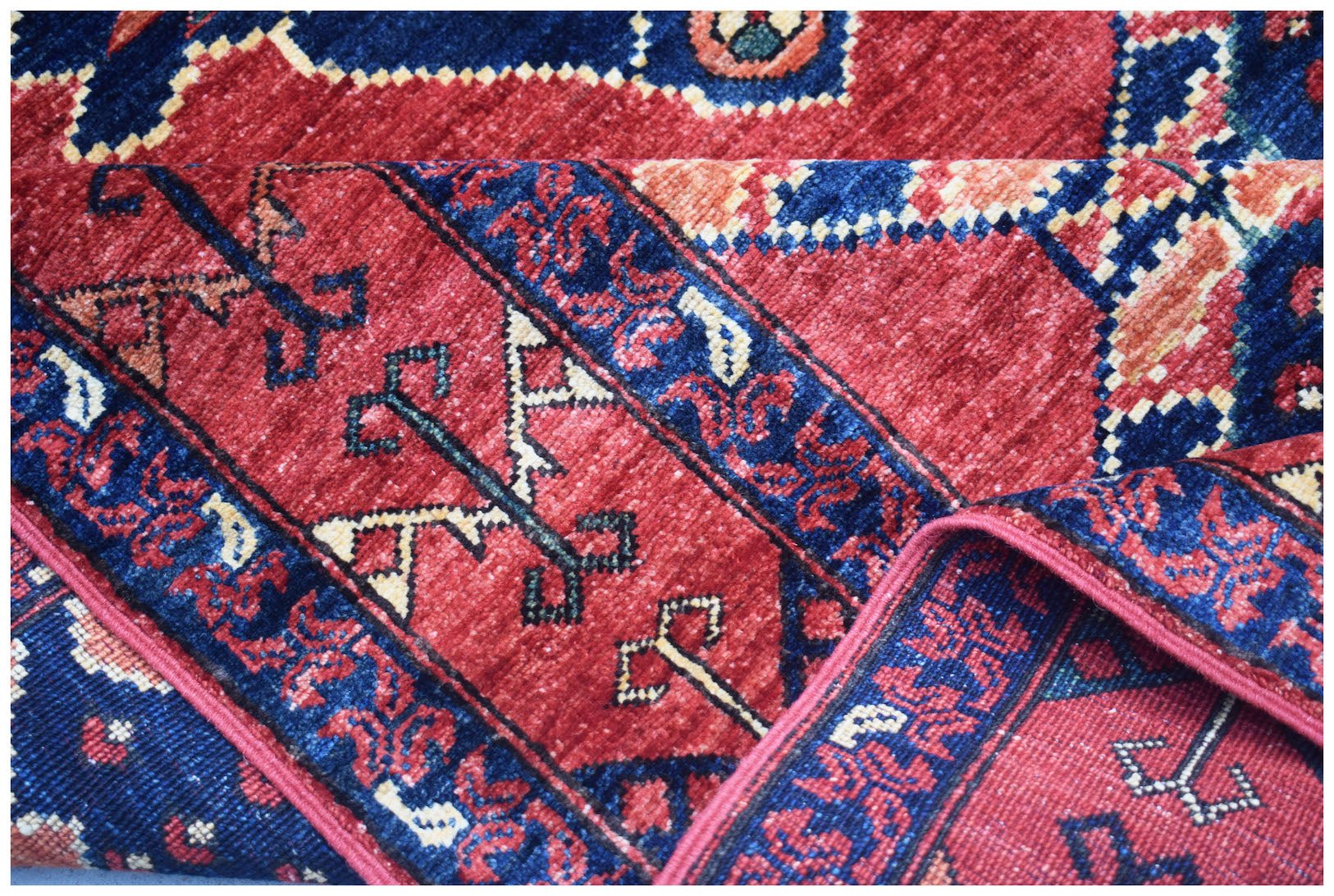 A handmade Afghan Chobi rug featuring a traditional geometric pattern in deep red and blue tones.