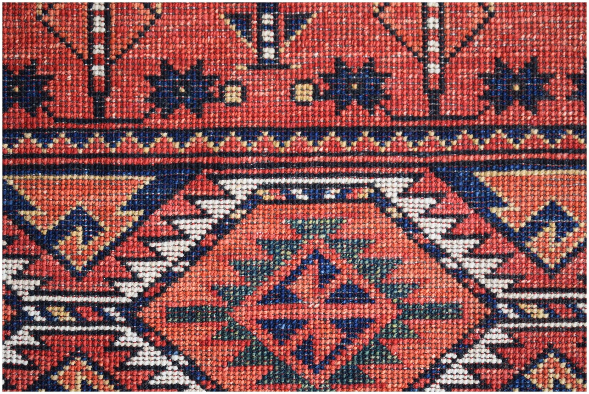 A close-up of an Afghan Chobi rug featuring intricate geometric patterns in red, blue, and white.