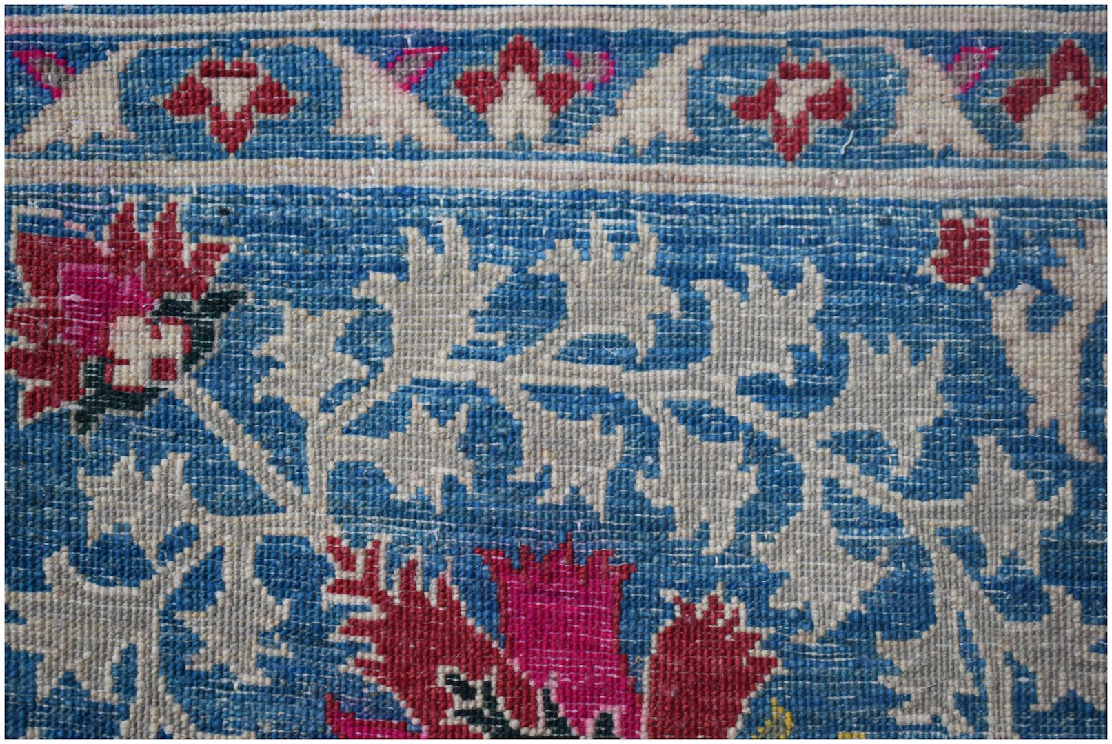 A close-up of an Afghan Chobi rug featuring intricate floral patterns in red, blue, and cream.