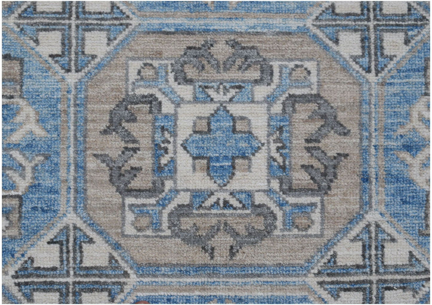 A handmade Afghan Chobi rug featuring a geometric medallion pattern in blue, beige, and grey.