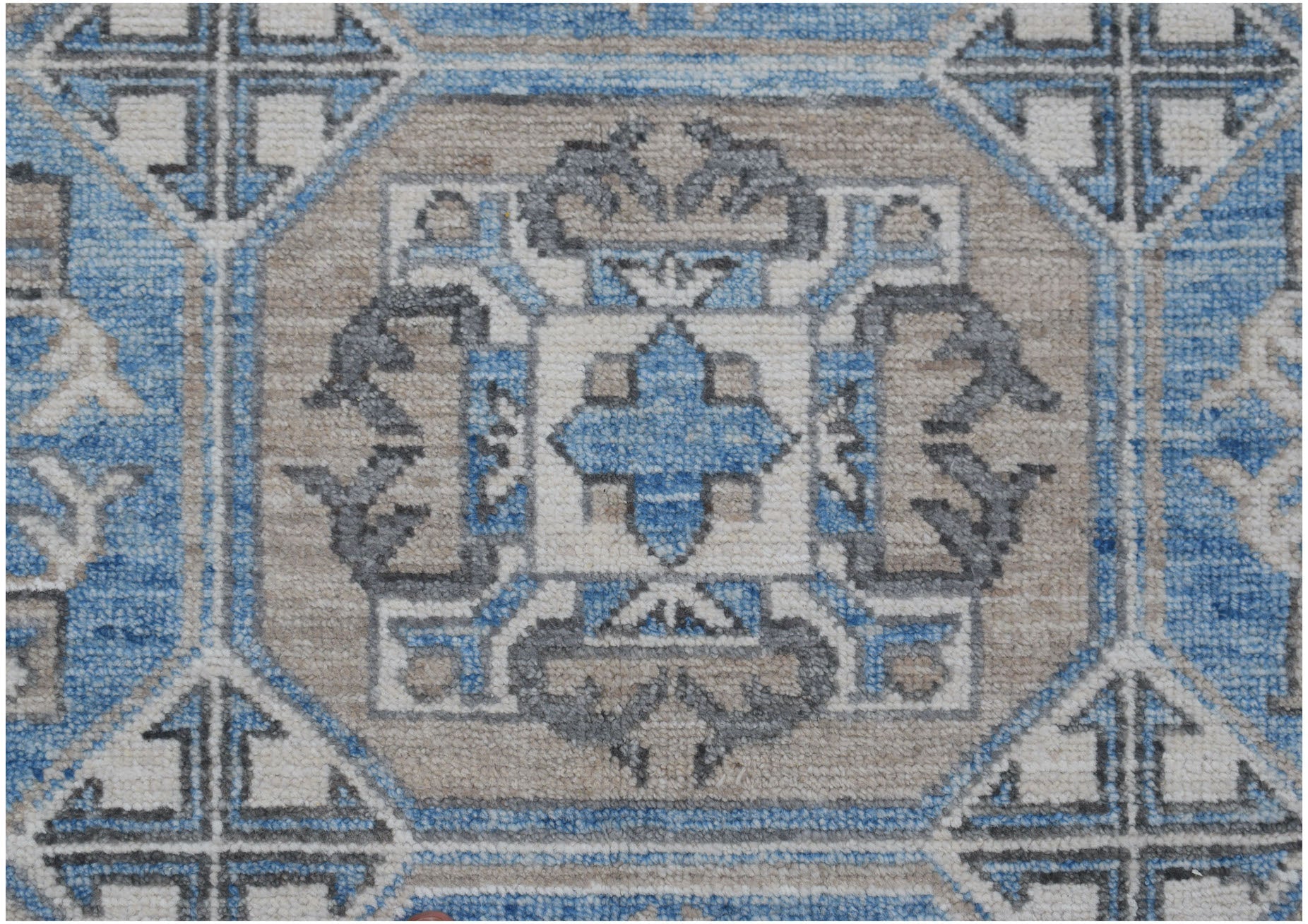 A handmade Afghan Chobi rug featuring a geometric medallion pattern in blue, beige, and grey.