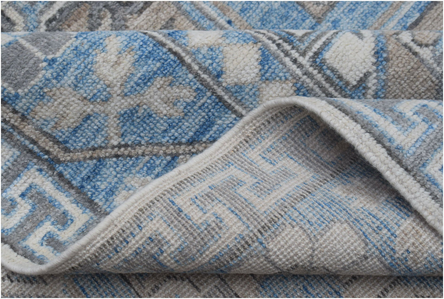 A close-up of a handmade Afghan Chobi rug featuring a blue, grey, and cream geometric pattern.