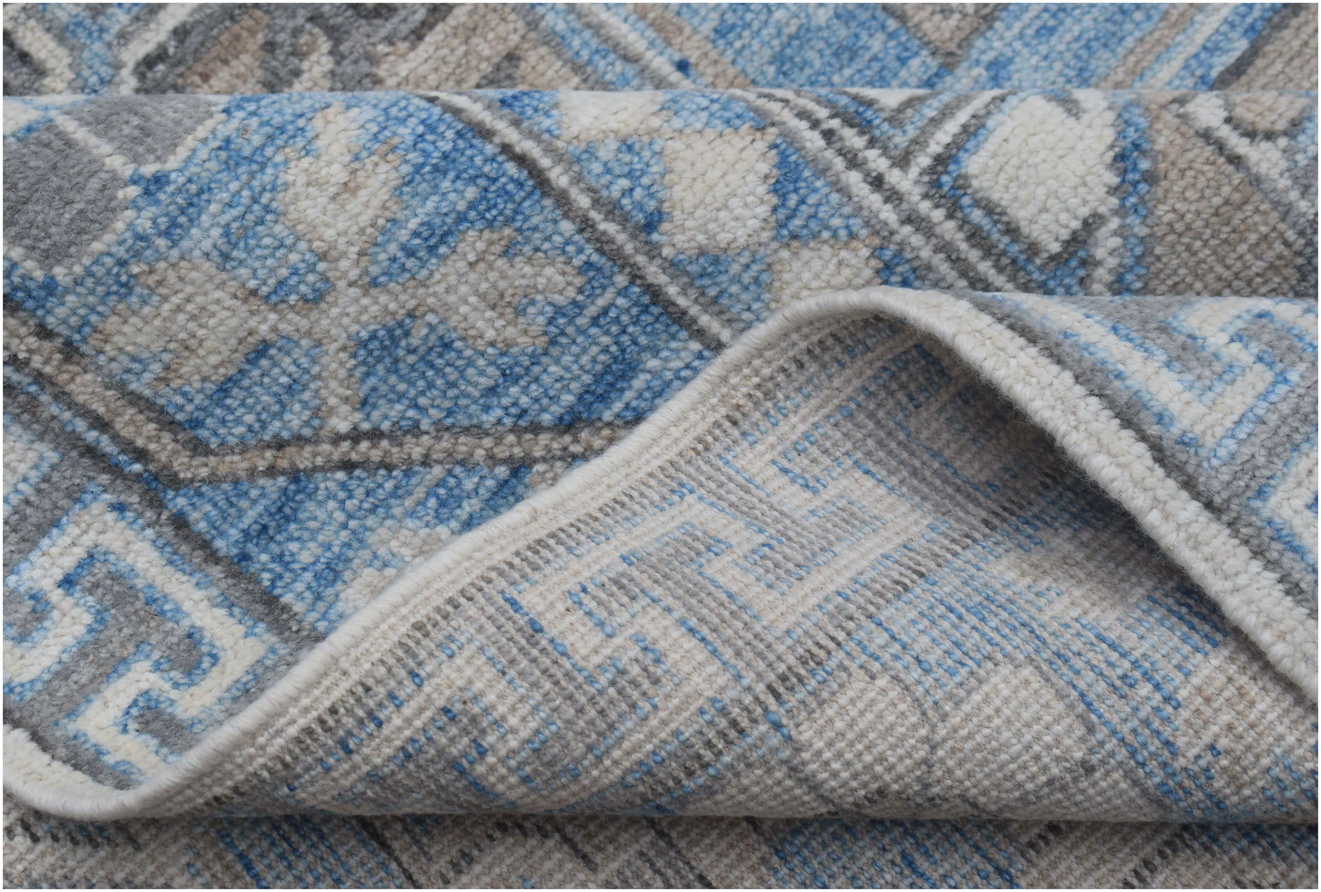 A close-up of a handmade Afghan Chobi rug featuring a blue, grey, and cream geometric pattern.