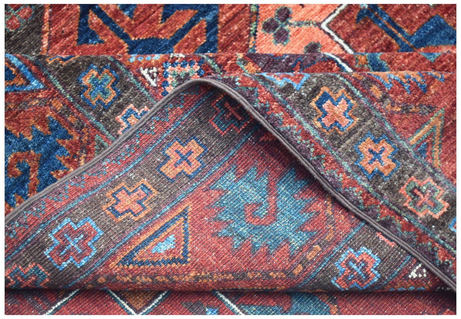A handwoven Afghan Chobi rug featuring a traditional geometric pattern in red, blue, and brown.