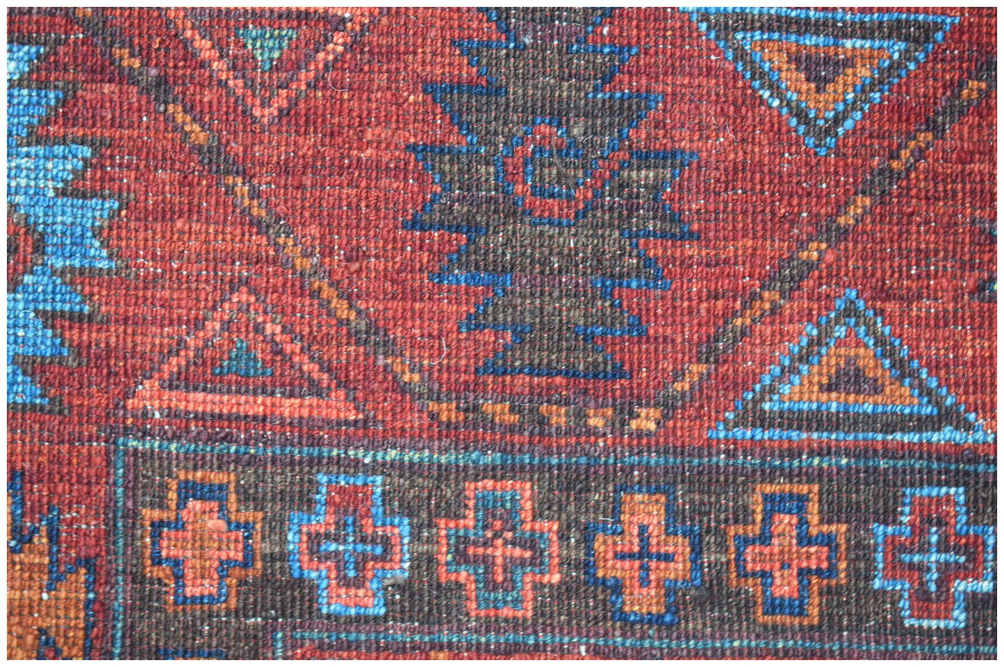 A close-up of a handwoven Afghan Chobi rug featuring geometric patterns in red, blue, and orange.