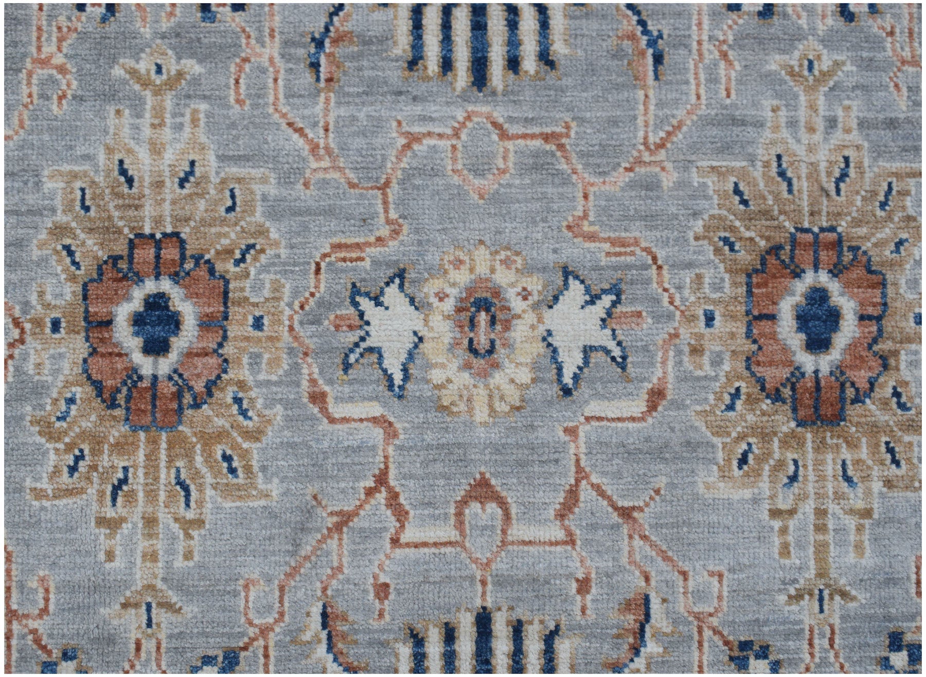 An Afghan Chobi rug featuring a traditional floral pattern in blue, tan, and rust on a grey field.