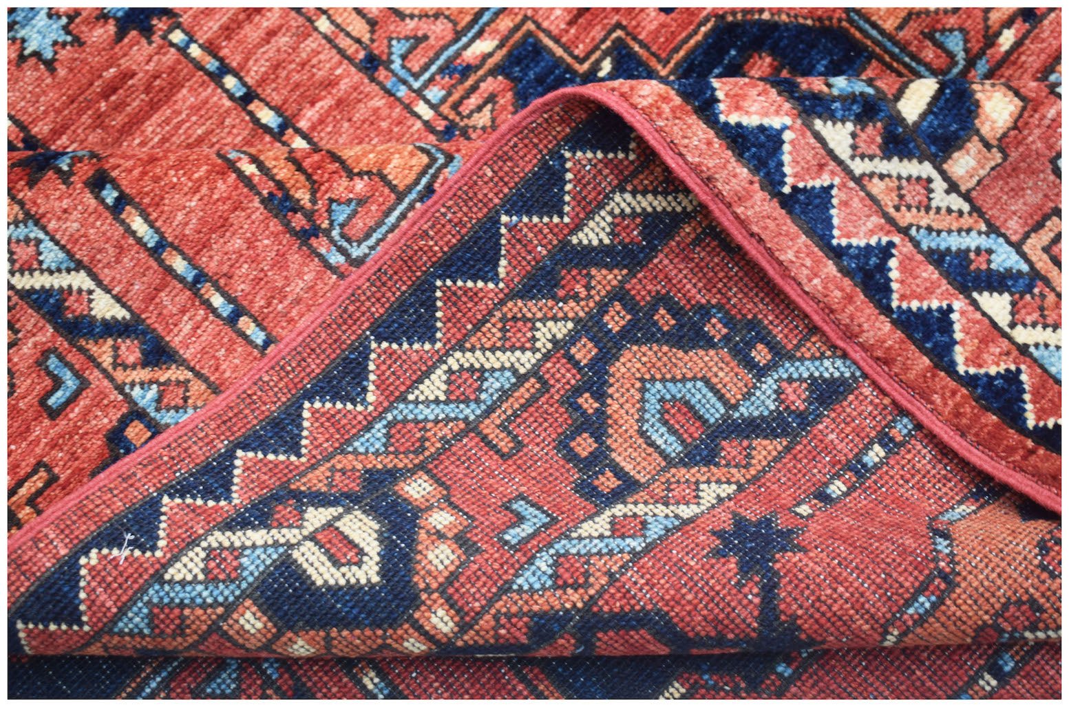 A corner of a handmade Afghan Chobi rug featuring traditional geometric patterns in red and blue.