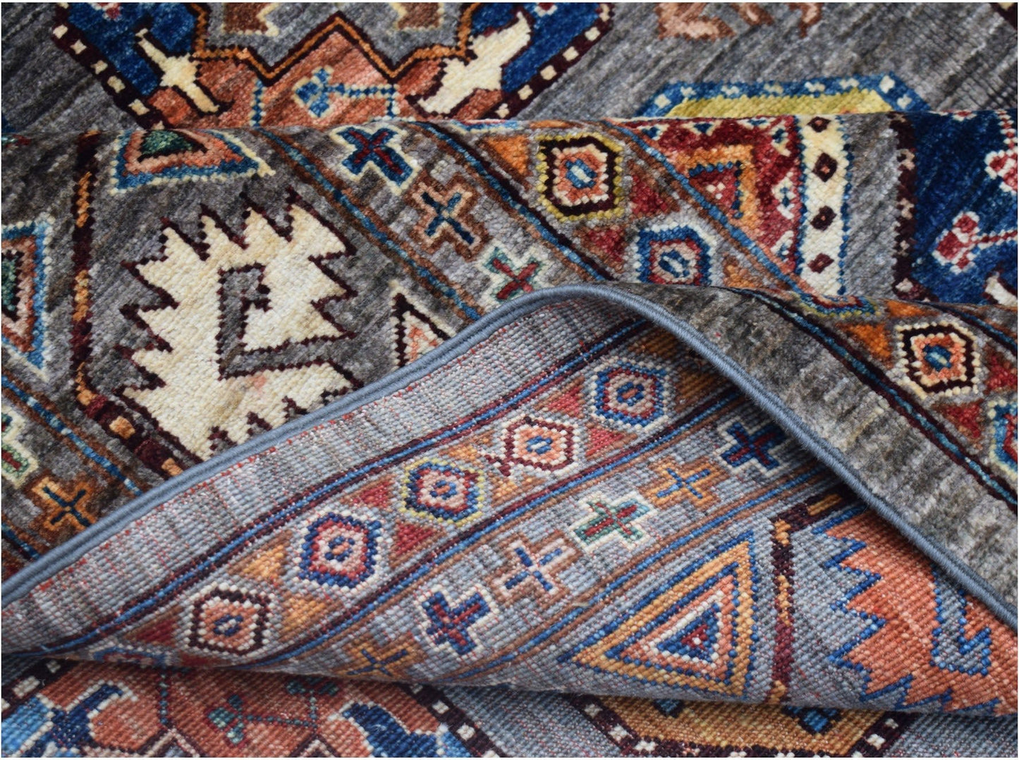 A folded Afghan Chobi rug featuring intricate geometric patterns in earthy tones and blue.