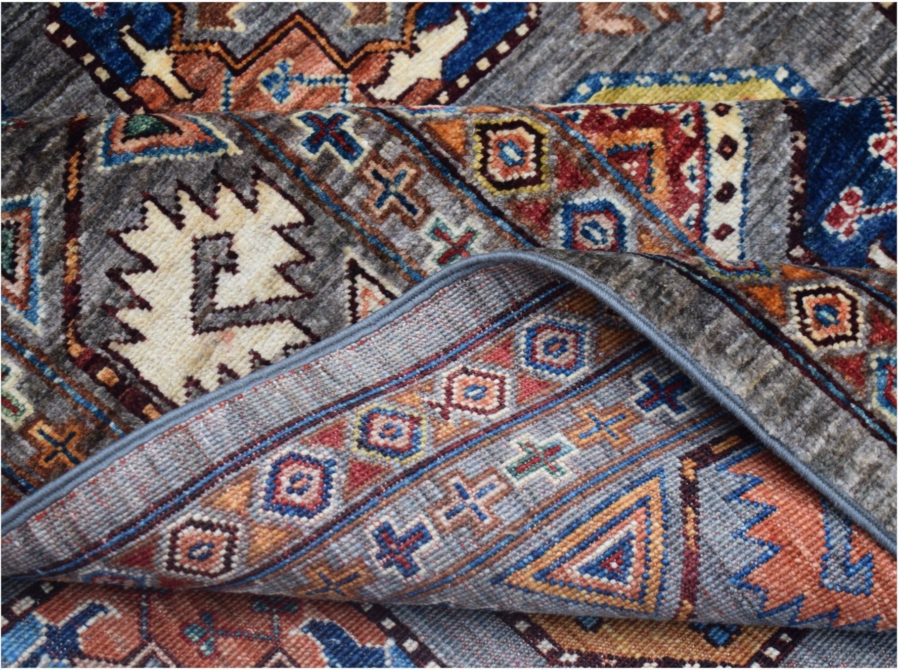 A folded Afghan Chobi rug featuring intricate geometric patterns in earthy tones and blue.