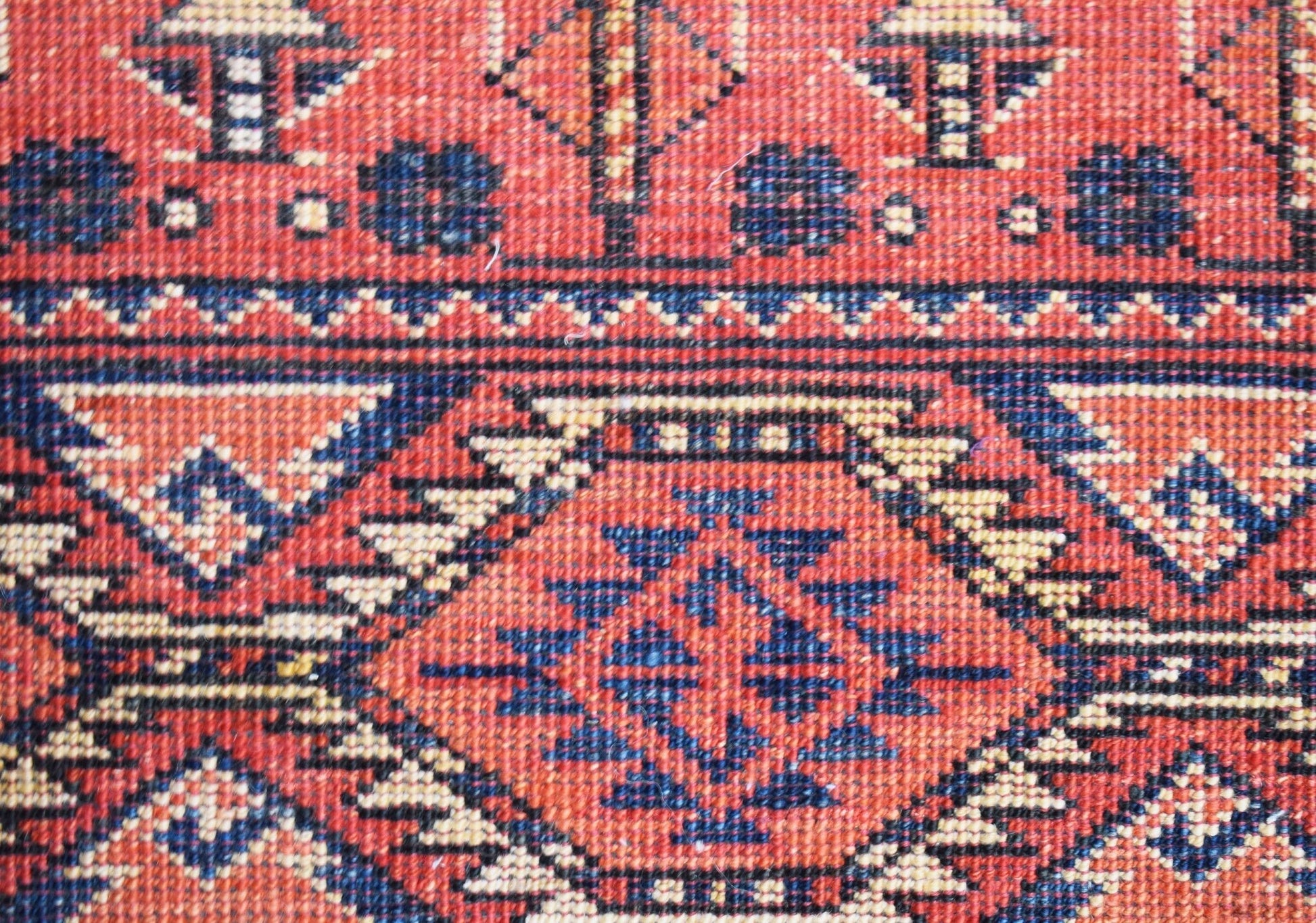 A close-up of a handmade Afghan Chobi rug featuring traditional geometric patterns in red and blue.