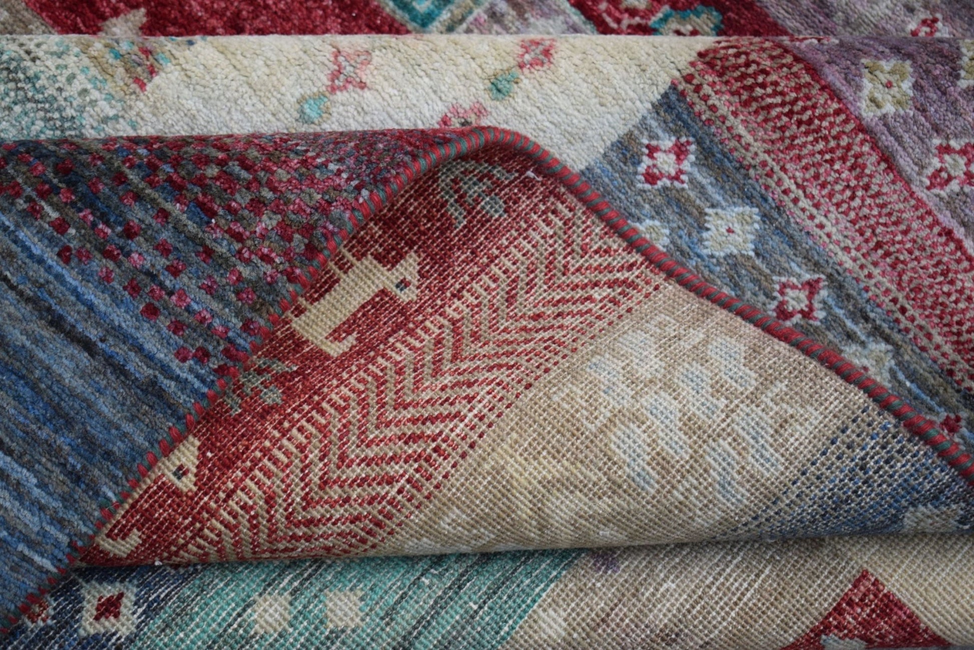 A folded Afghan Chobi rug featuring intricate geometric patterns in red, blue, and beige tones.