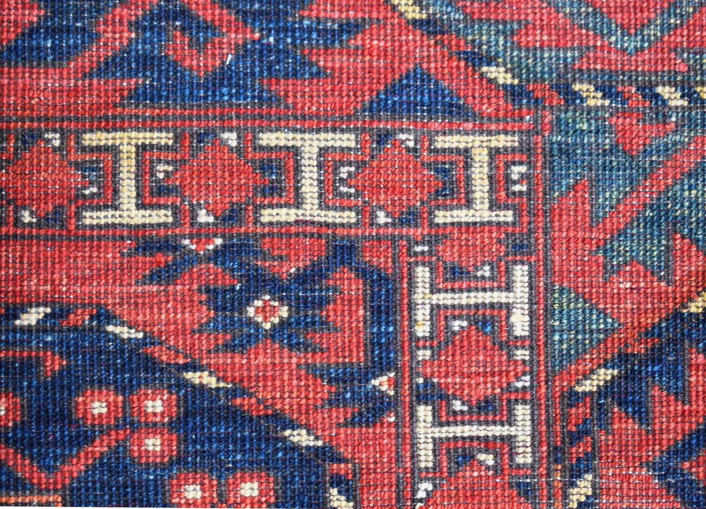 A close-up of a handwoven Afghan Chobi rug featuring a geometric border pattern in red and blue.