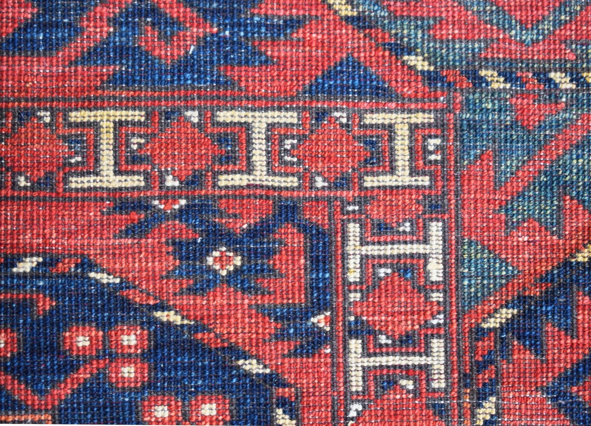 A close-up of a handwoven Afghan Chobi rug featuring a geometric border pattern in red and blue.