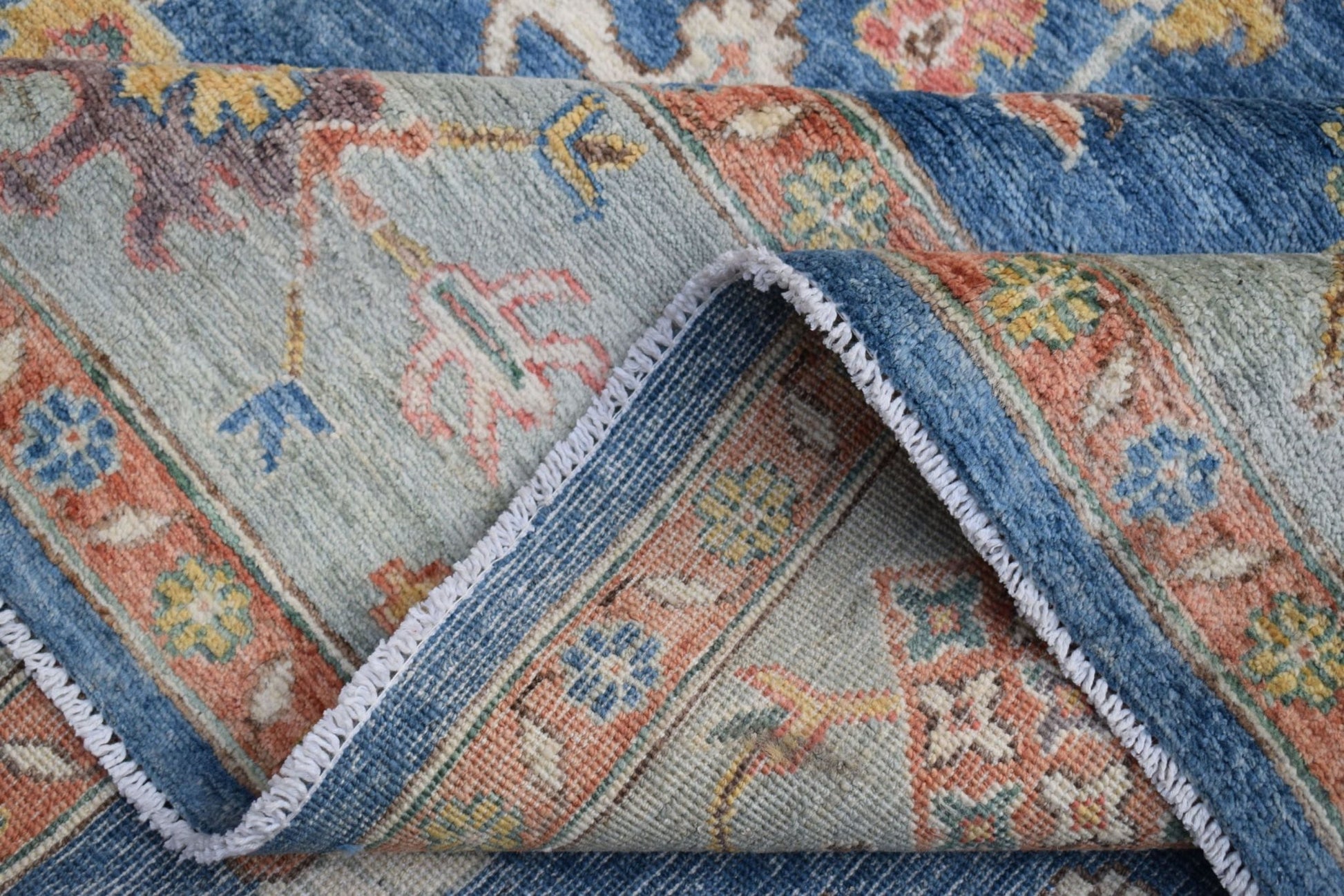 A folded Afghan Chobi rug featuring traditional floral patterns in blue, peach, and cream tones.