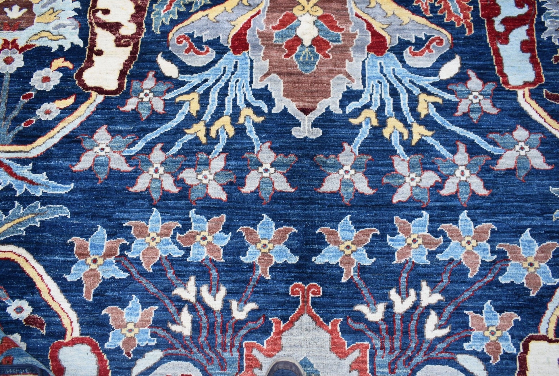 A handwoven Afghan Chobi rug featuring a traditional floral pattern in blue and earthy tones.